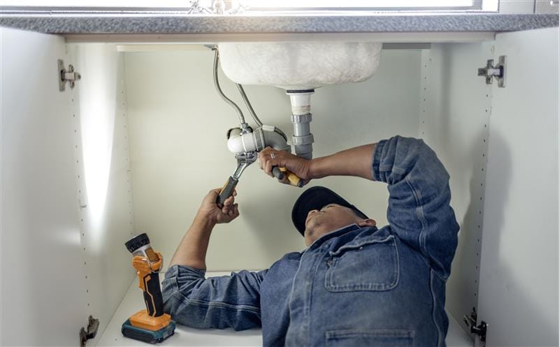 Plumber repairing pipes beneath a bathroom sink in Casselberry