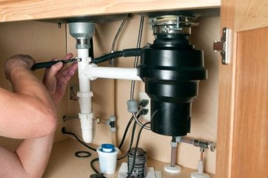 Plumber repairing a garbage disposal beneath a kitchen sink in Casselberry
