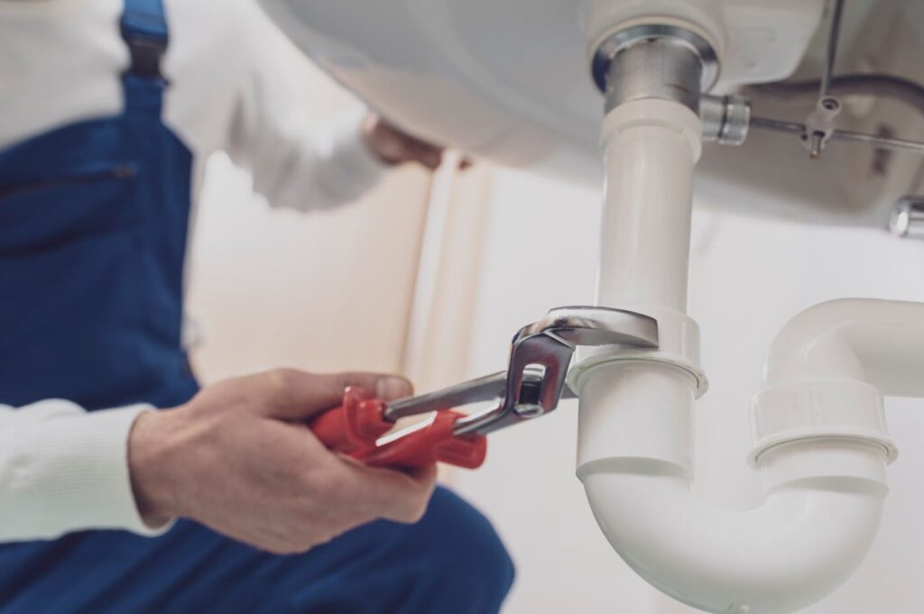 Plumber repairing a white drain pipe beneath a sink in Casselberry